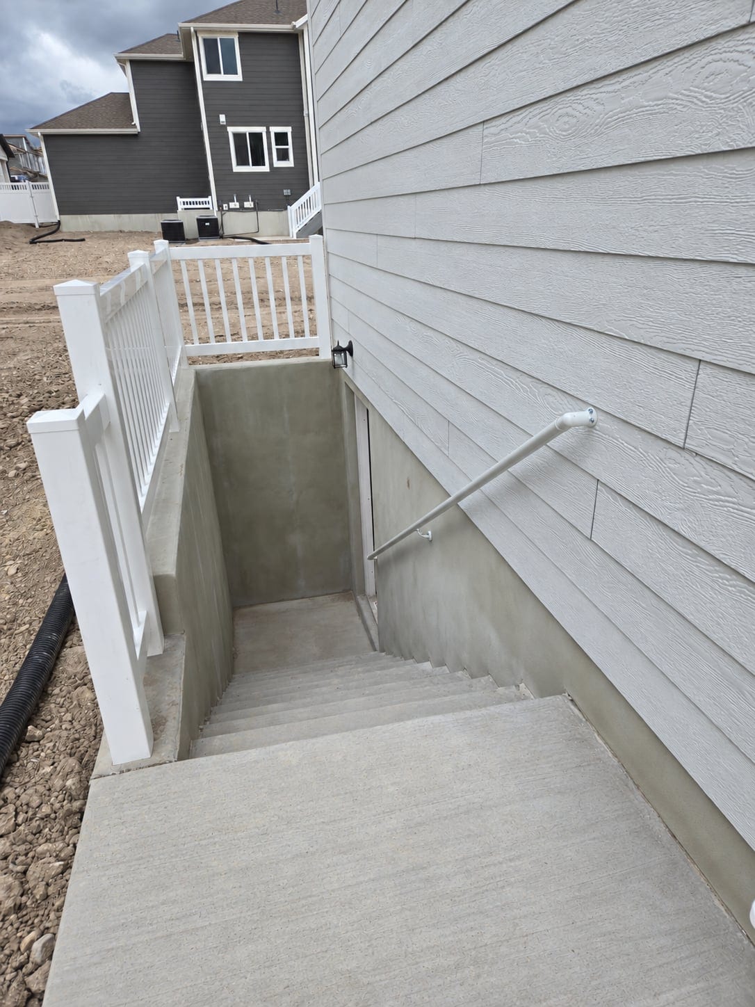 Exterior basement stairs with white perimeter railing and a wall-mounted handrail