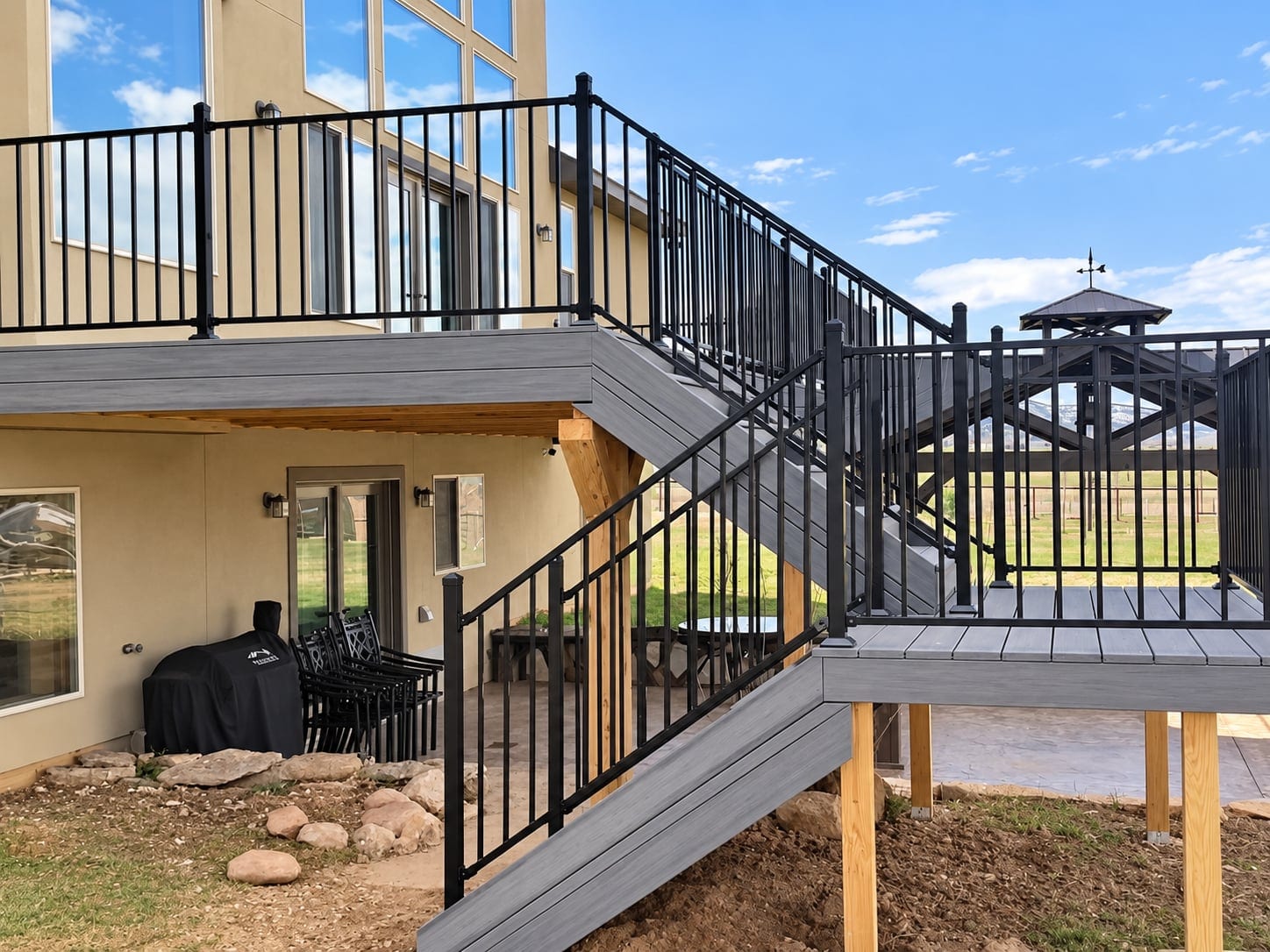 Raised gray deck with stairs, a landing, and black metal railings beside a home